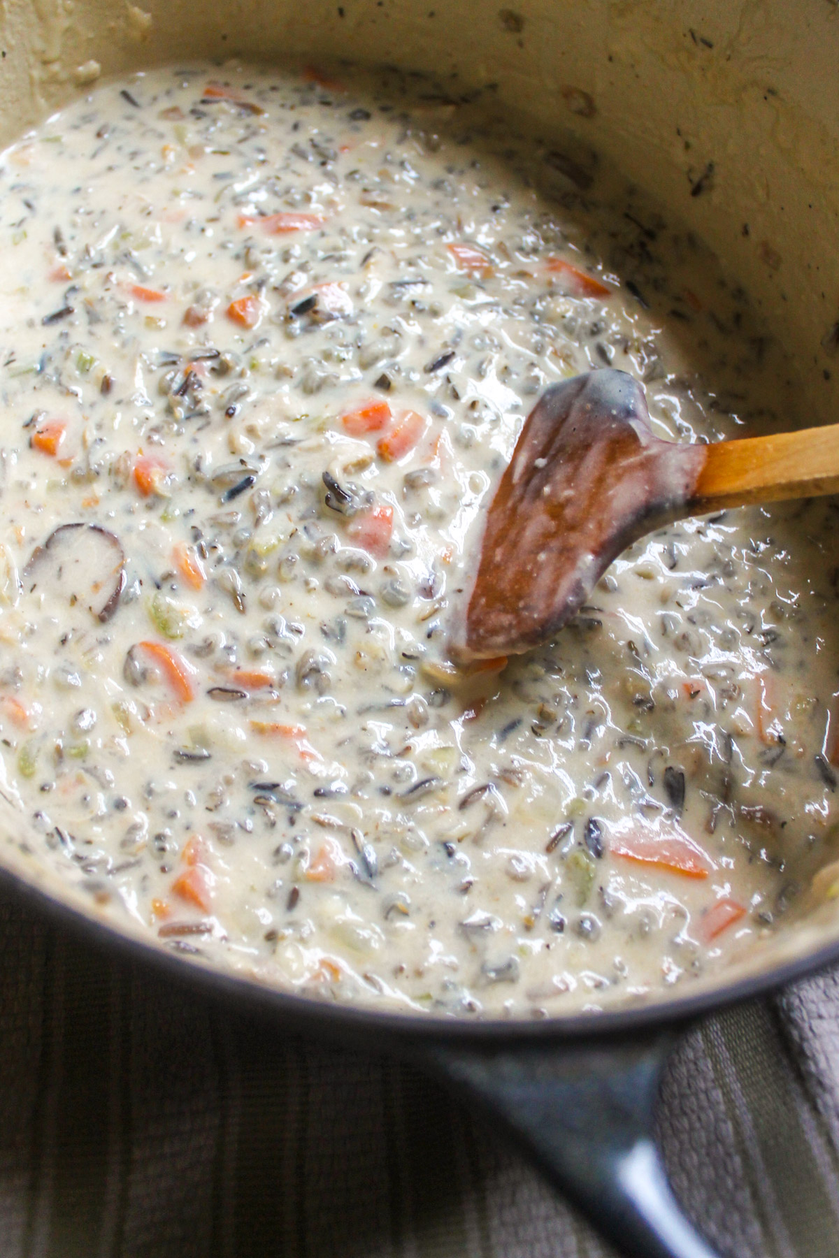 A pot of chicken wild rice soup with a wooden spoon.