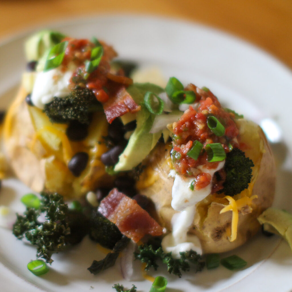 Loaded baked potatoes topped with cheese, broccoli, avocado, bacon, black beans, corn, salsa and scallions.