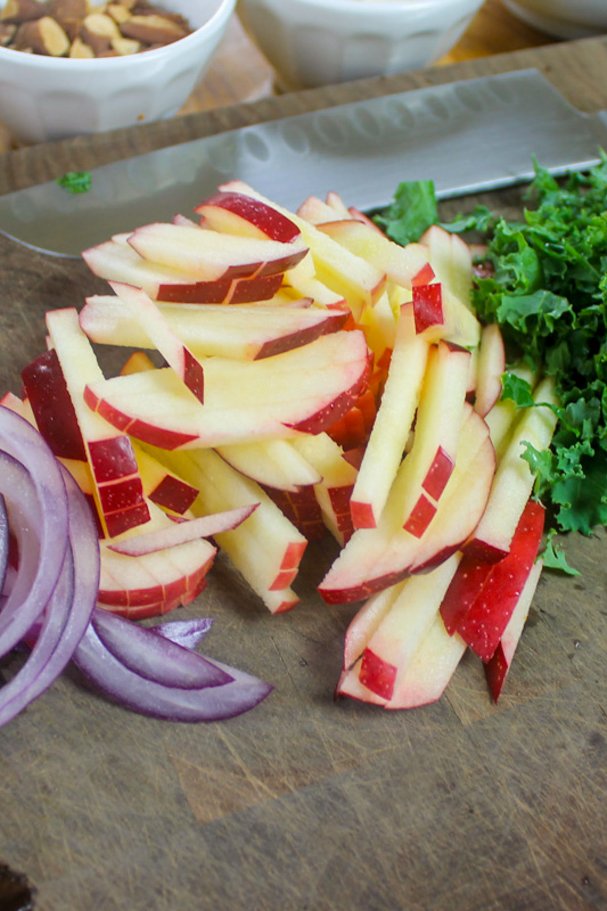 Slice kale, red onion and julienne apples on a cutting board.