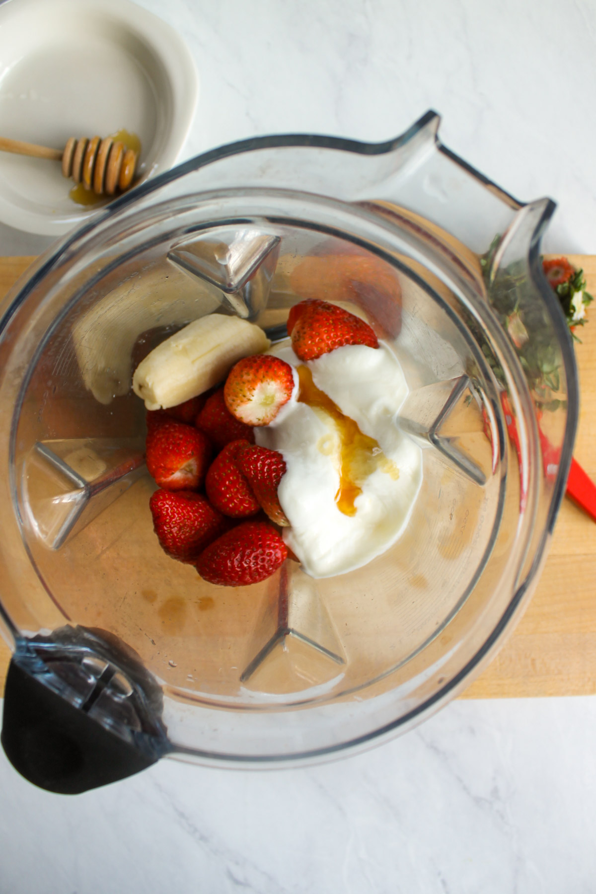 A blender with banana, strawberries, yogurt and honey.