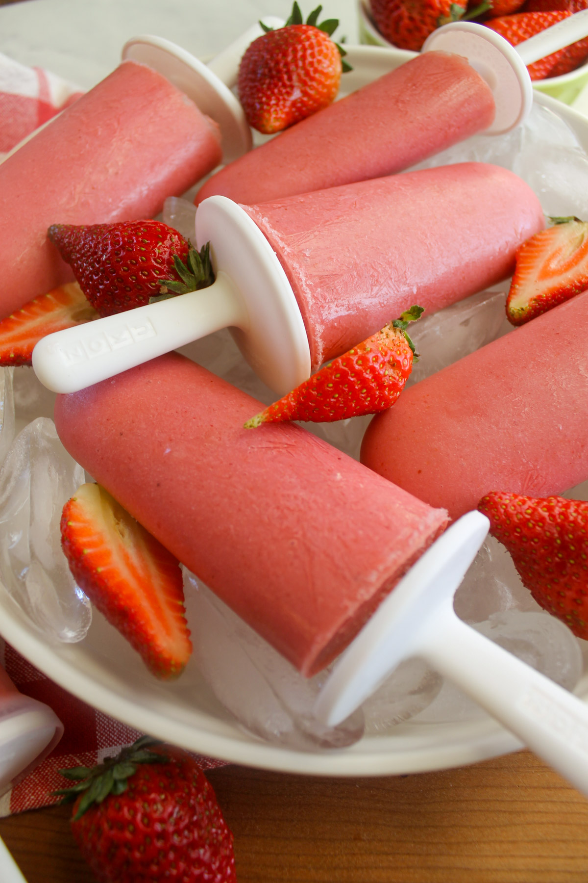 Homemade Strawberry Popsicles with white handles on a bed of ice.