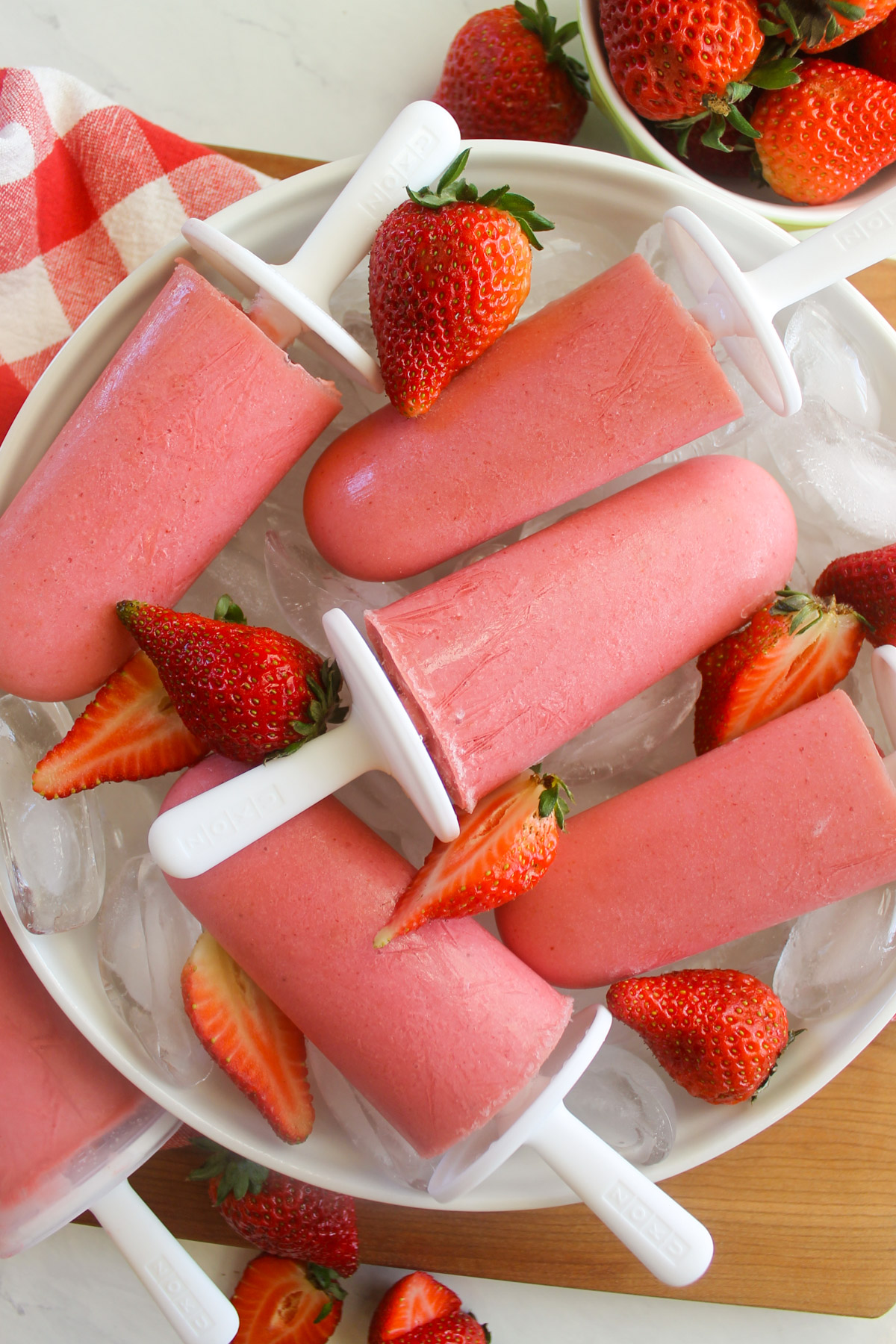 Strawberry Banana Yogurt Popsicles on ice with fresh sliced strawberries.