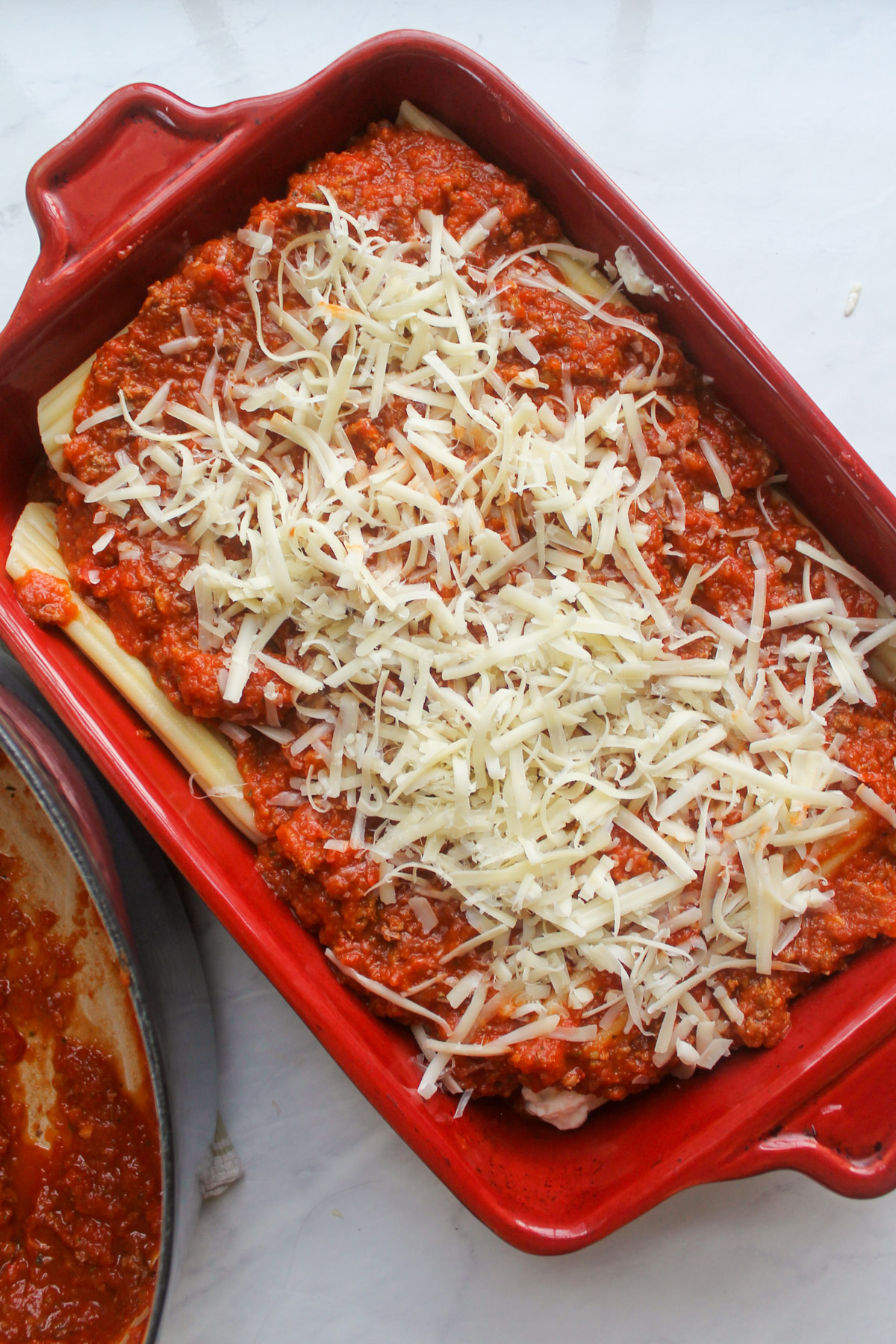 Manicotti topped with meat sauce and white shredded cheese ready to bake.
