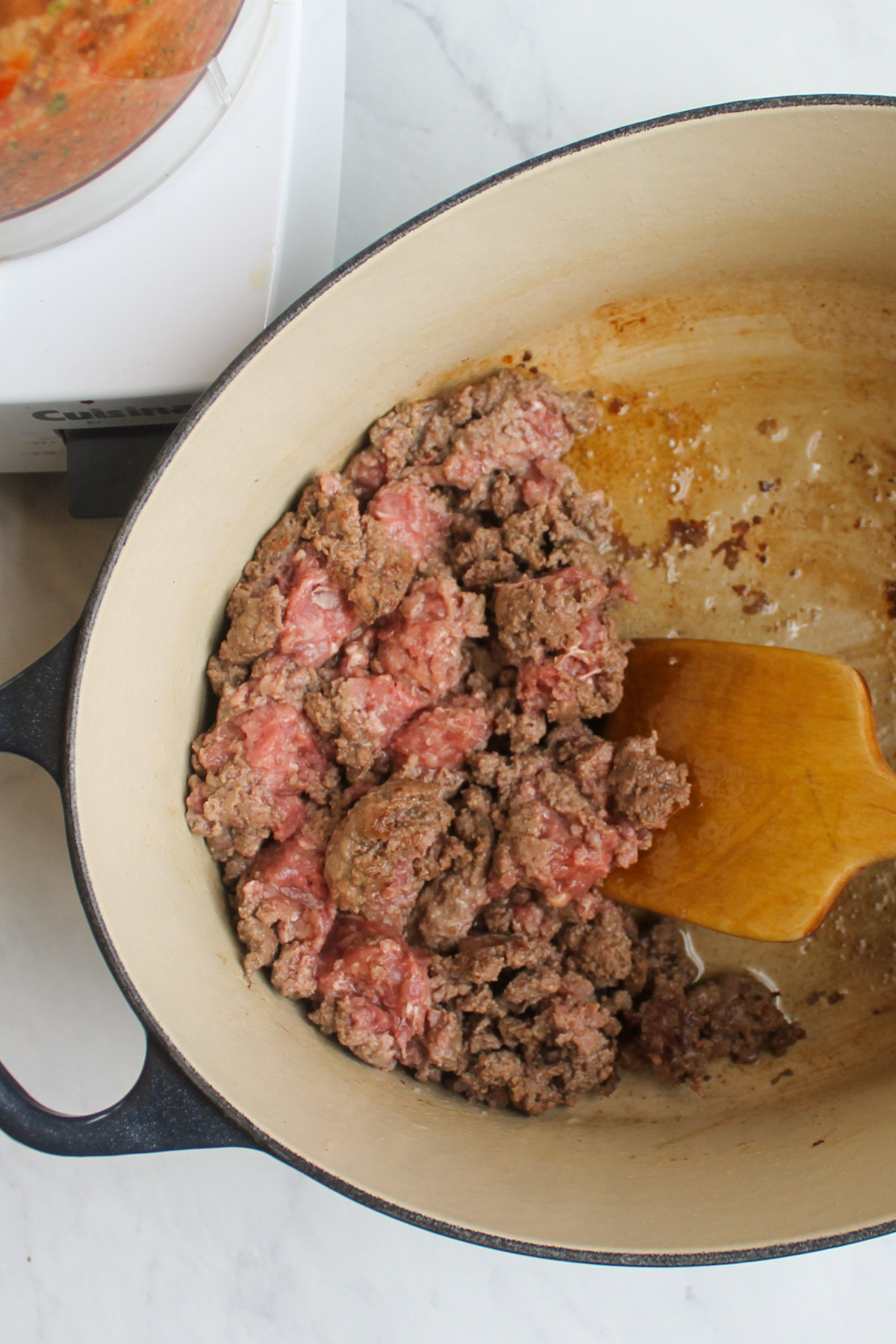 Browning ground beef in a pot with a wooden spoon.