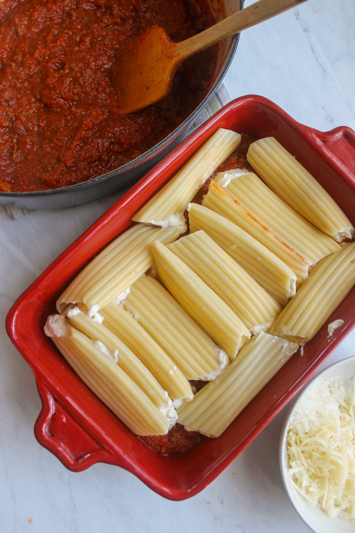 Manicotti noodles stuffed with cheese filling and lined up in the sauce in a pan.
