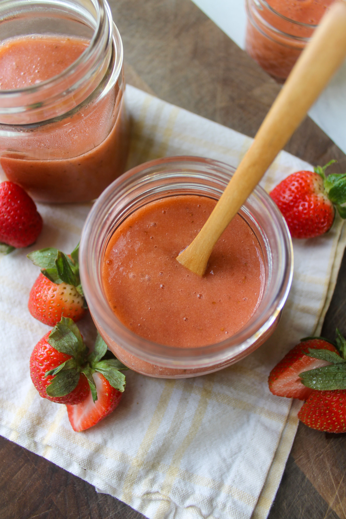 A jar of pink strawberry rhubarb sauce with a small wooden spoon.
