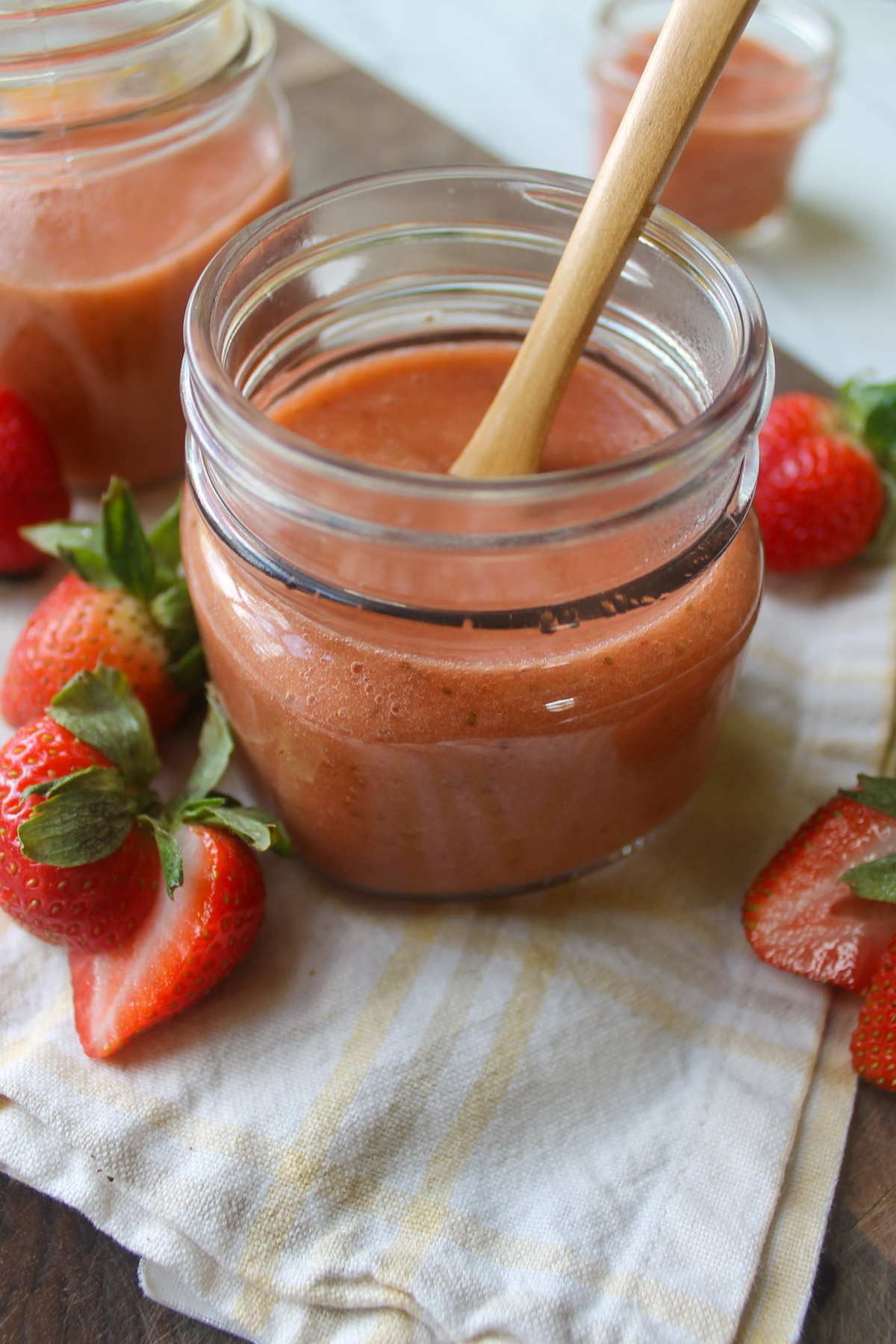 A jar of strawberry rhubarb sauce with fresh strawberries on a cutting board.