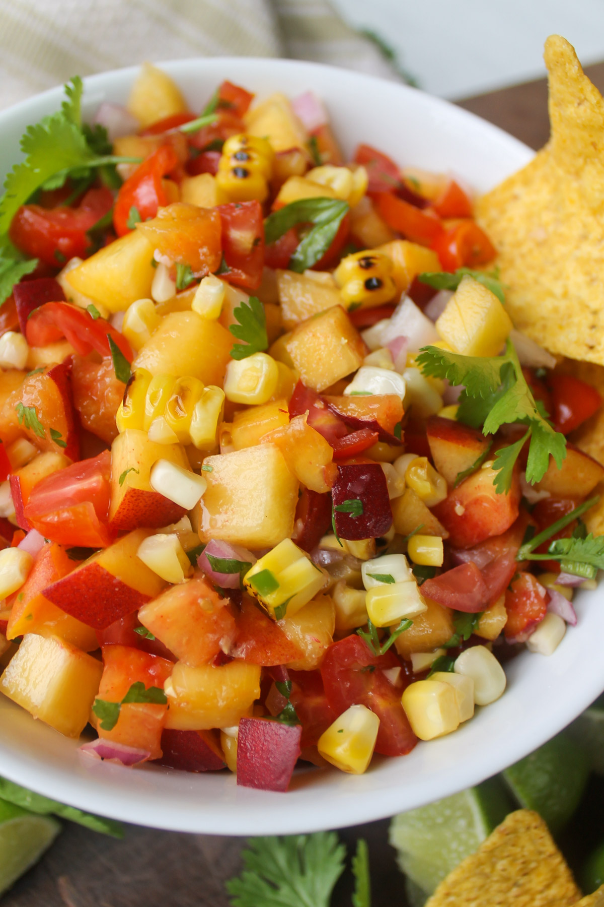 A white bowl of peach corn salsa with cherry tomatoes.