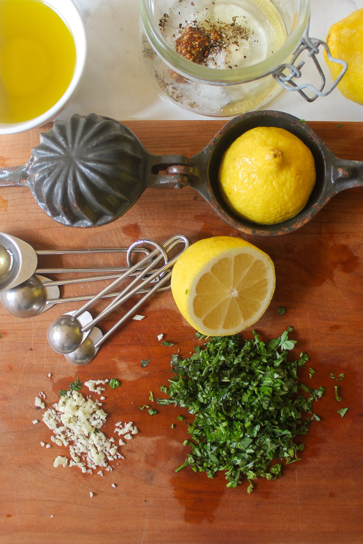 A cutting board with chopped fresh herbs, a lemon cut in half and minced garlic.