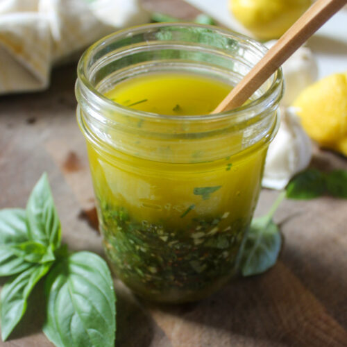 A jar of vinaigrette with yellow olive oil and lemon juice and lots of fresh garden herbs.