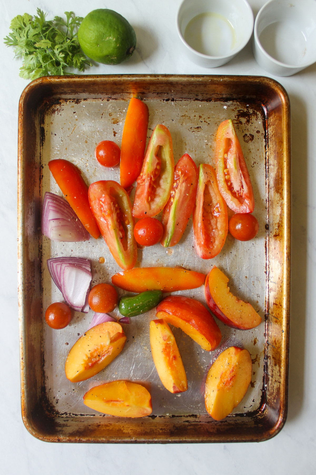 Raw tomato, peach, onion and jalapeño pepper on a roasting pan.