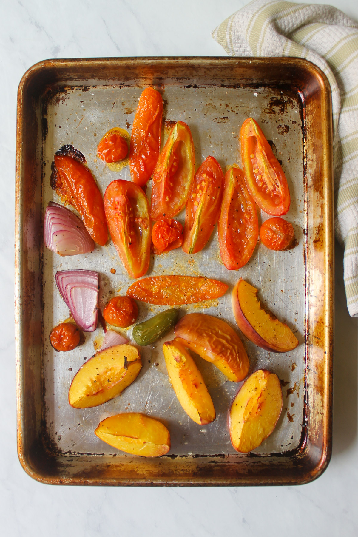 Roasted tomato, peach, onion and jalapeño pepper on a sheet pan.