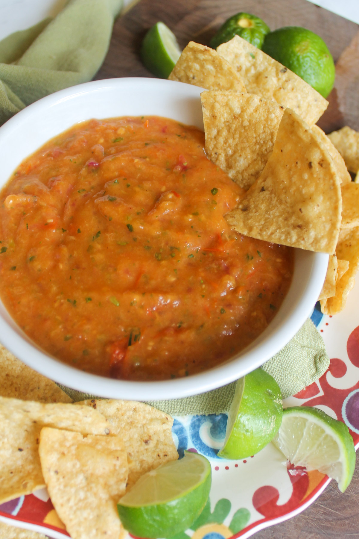 A white bowl of roasted peach salsa with chips and lime wedges.