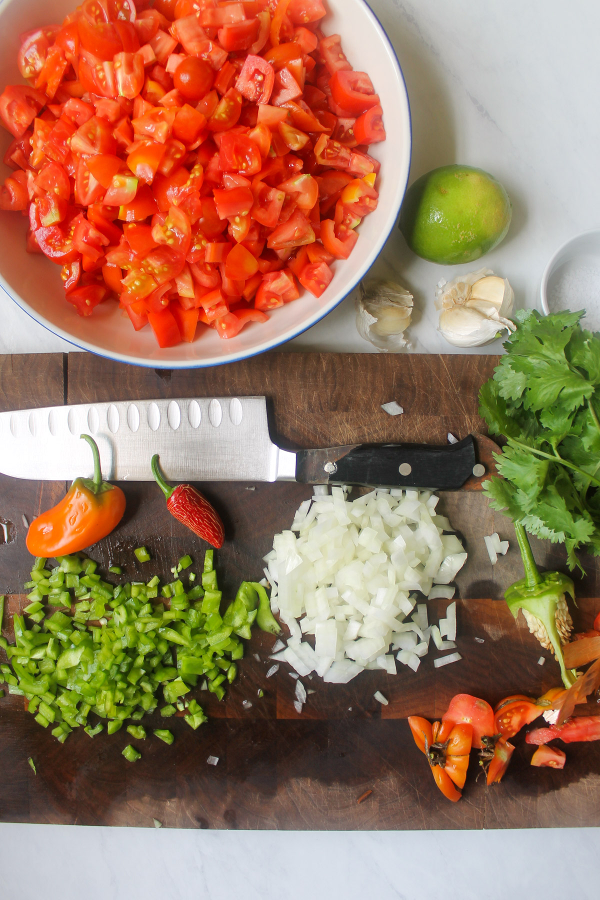 A bowl of chopped tomatoes and chopped onion and green peppers on a cutting board.