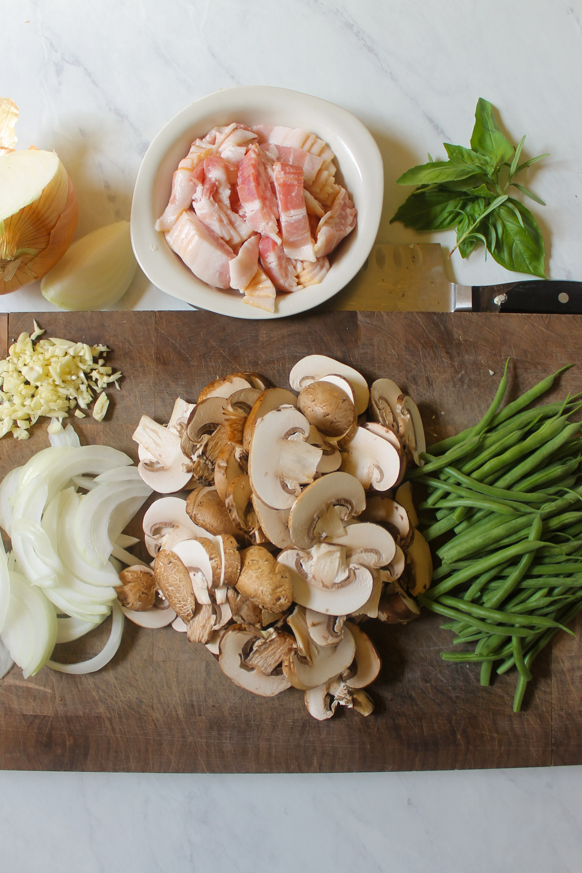 A cutting board with sliced mushrooms, onions, garlic and green beans.