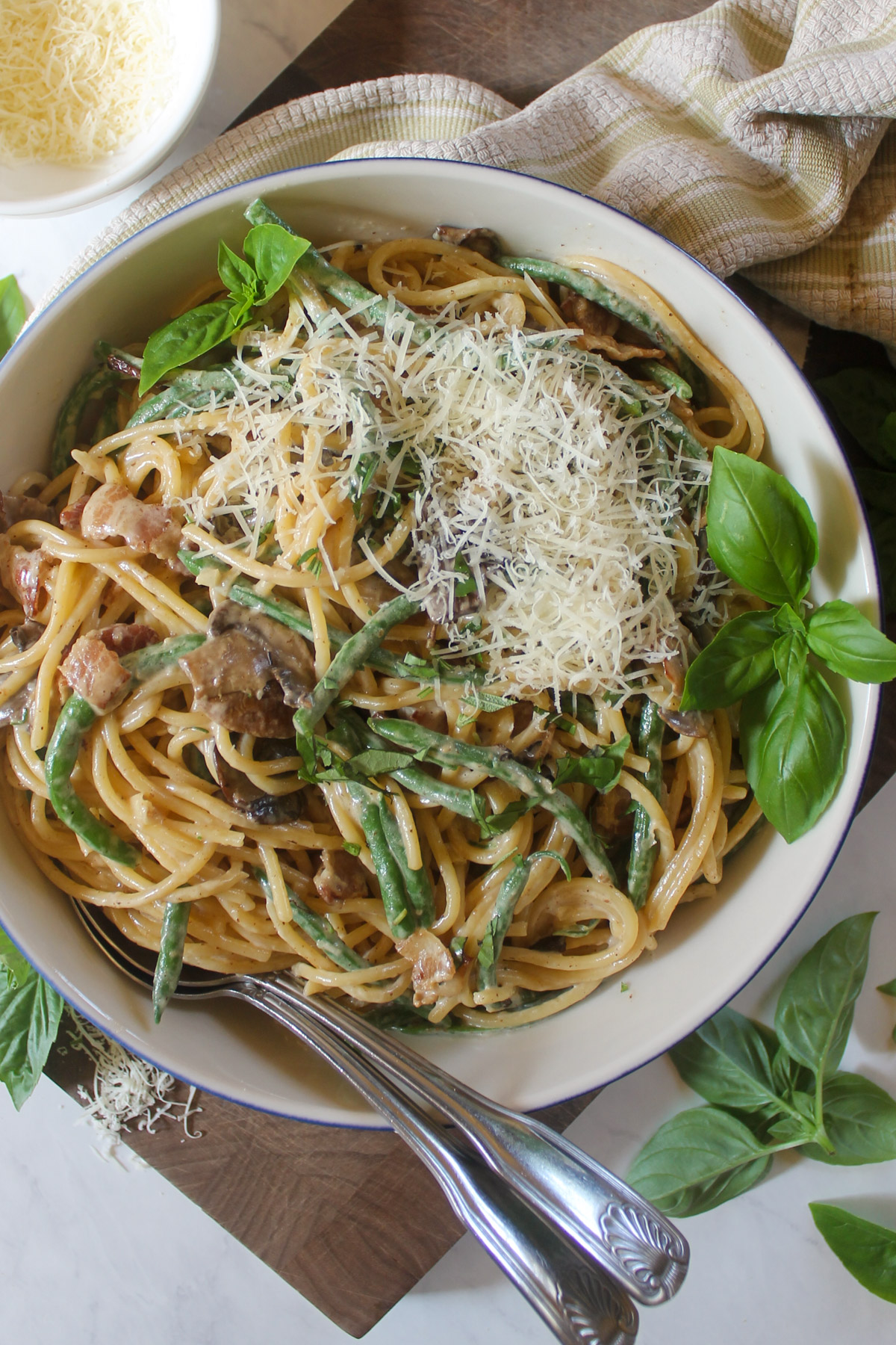 A bowl of green bean pasta with bacon and basil.