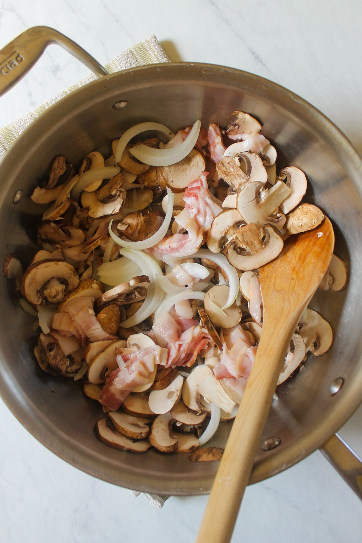 Raw bacon, onions and mushrooms sliced in a skillet.