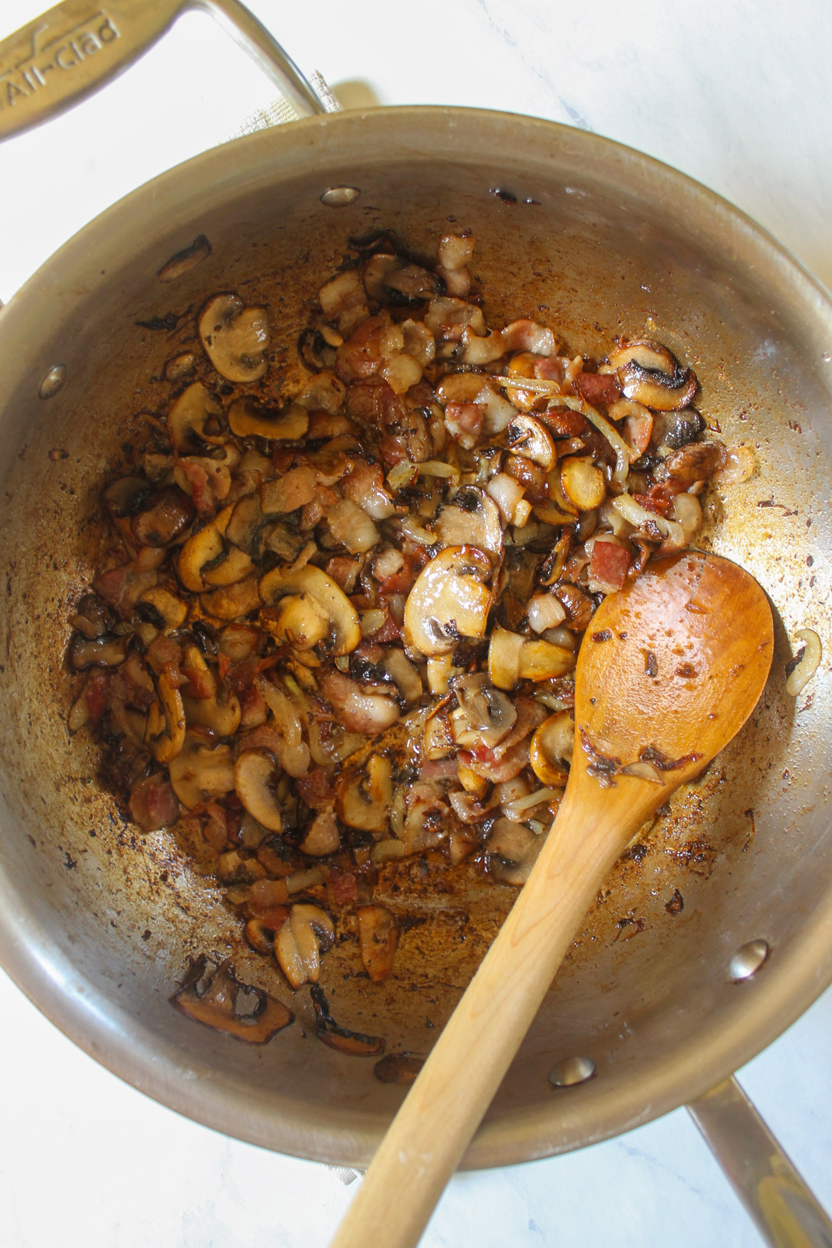 Cooked bacon, mushrooms and onions in a skillet.