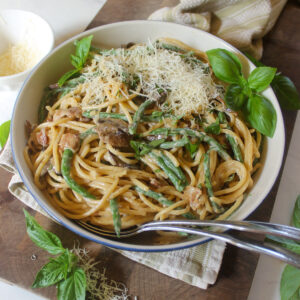 A bowl of spaghetti with green beans, mushrooms and Parmesan cheese.