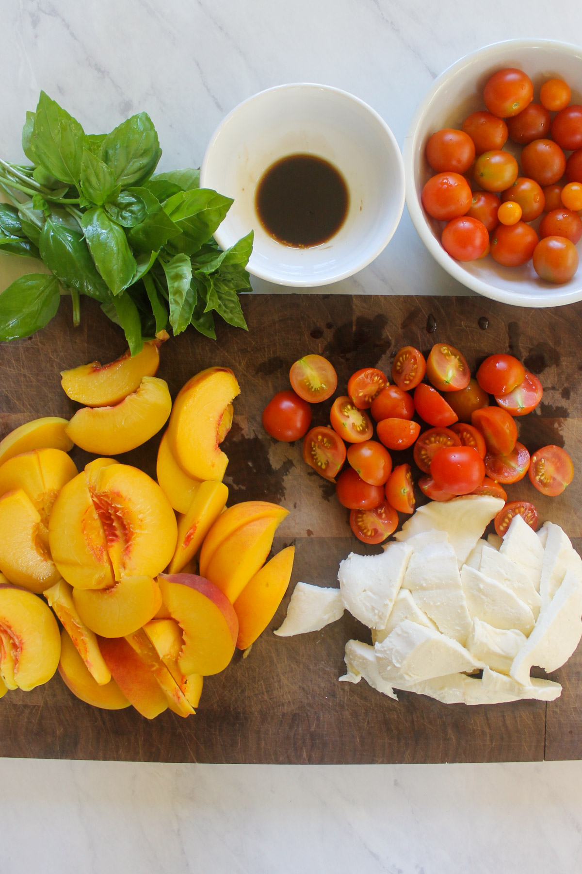 Sliced peaches, cherry tomatoes and fresh mozzarella cheese on a cutting board.