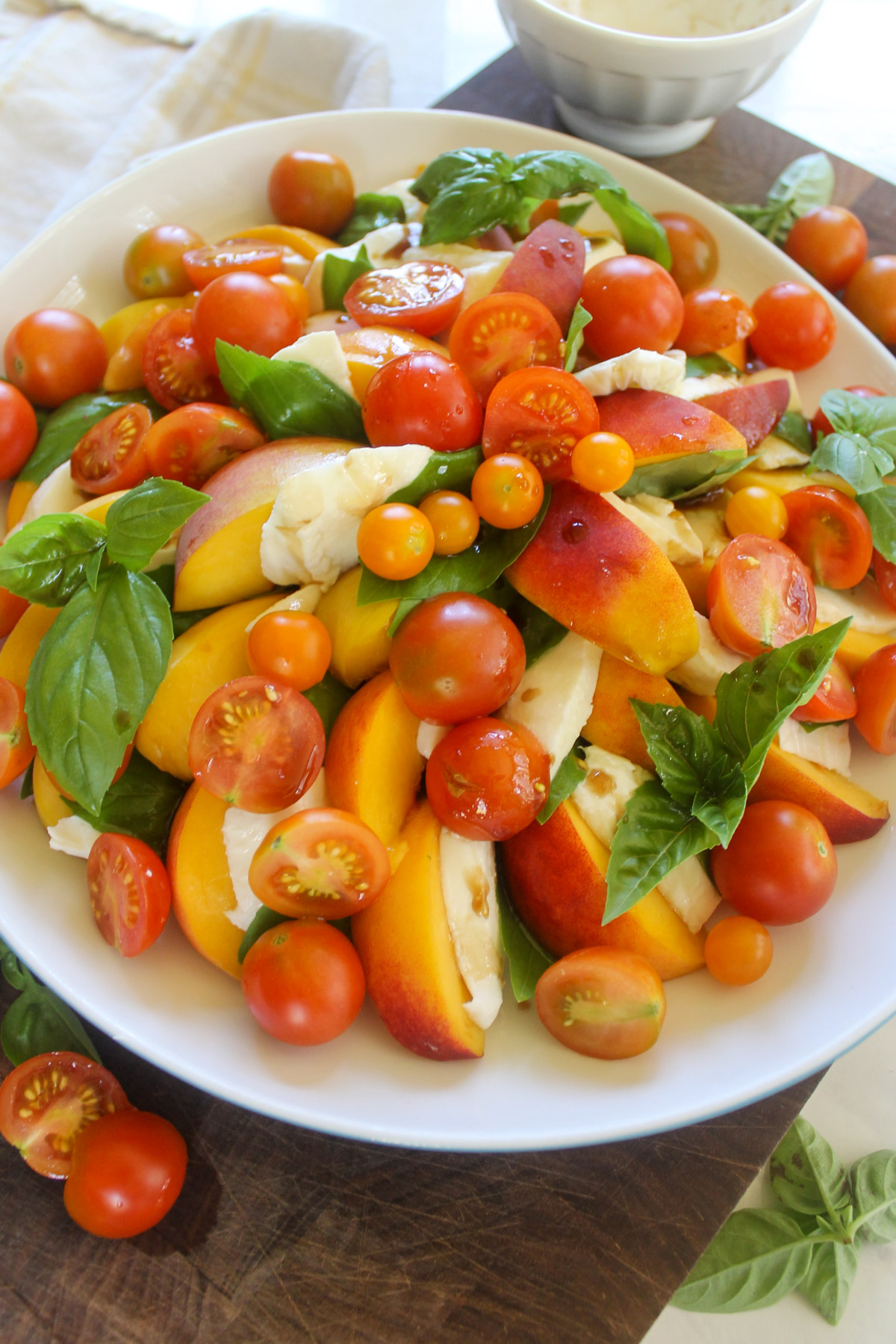 A white plate of sliced peaches, fresh mozzarella cheese, basil and cherry tomato.