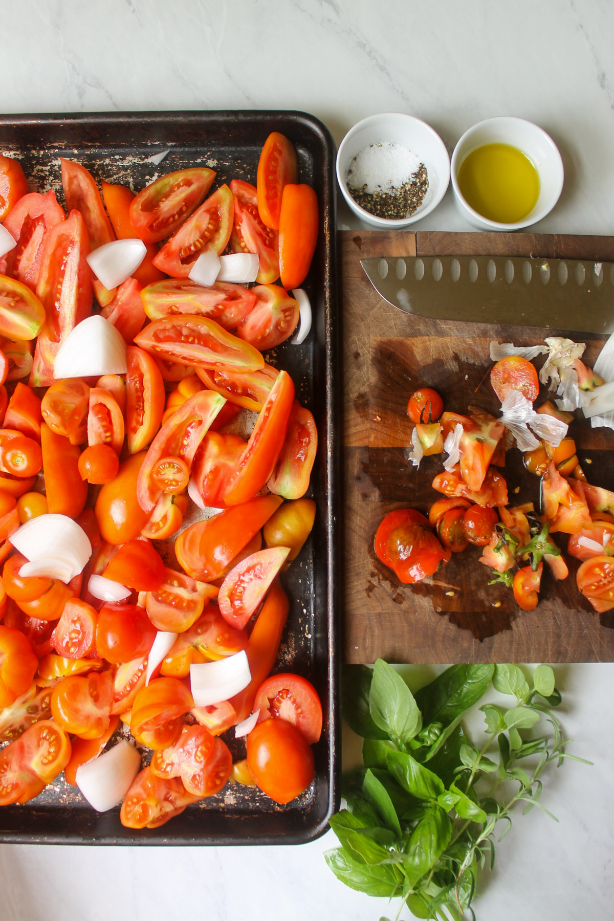 Slicing tomatoes on a cutting board and adding to a sheet pan with onions.