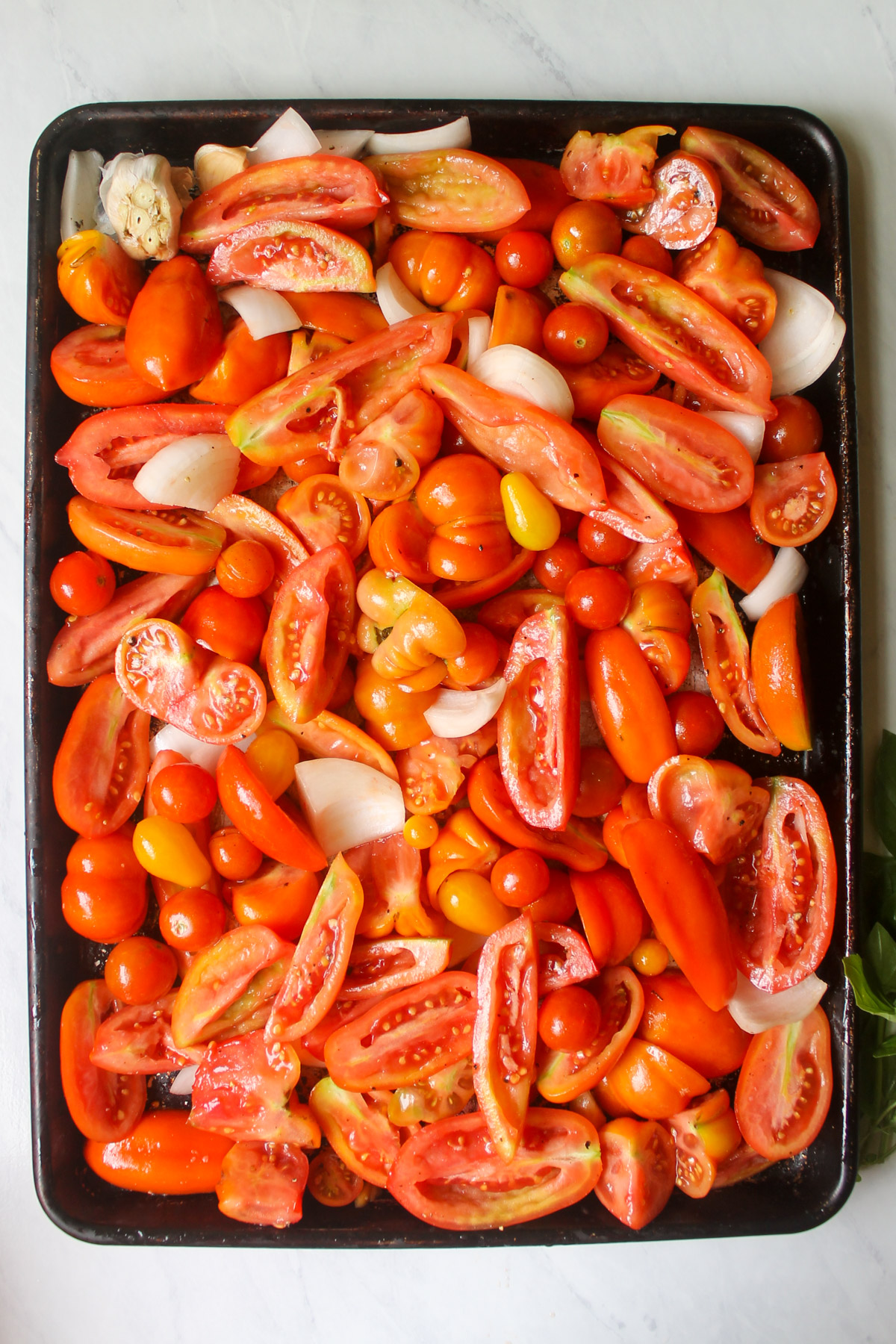 A large sheet pan of quartered tomatoes, onions and garlic.