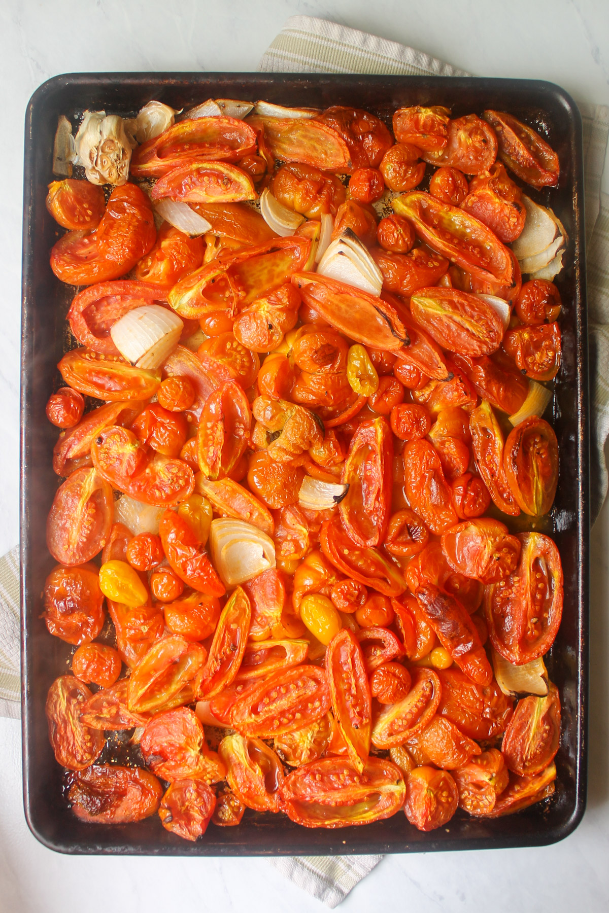 A large sheet pan of roasted tomatoes with onions and garlic.