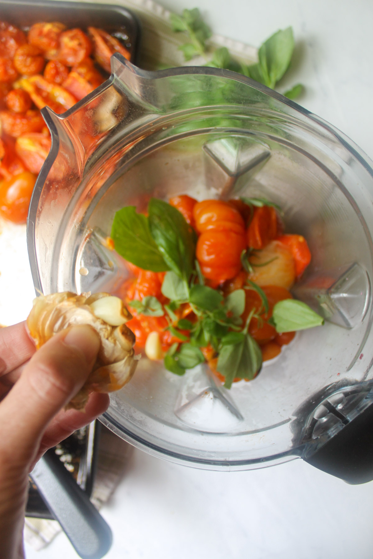 Adding roasted garlic and fresh herbs to tomatoes in a blender.