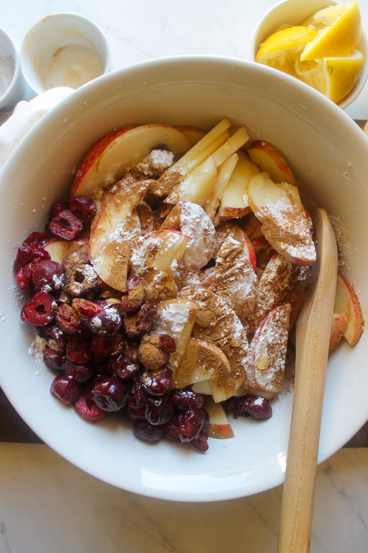 Mixing apple cherry crisp filling in a white bowl.