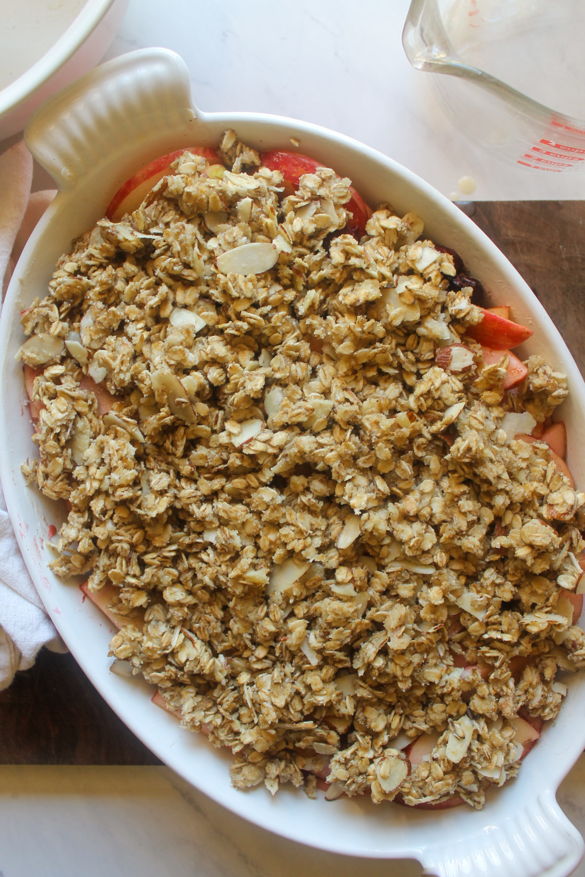 Unbaked apple cherry crisp in a white oval baking dish.