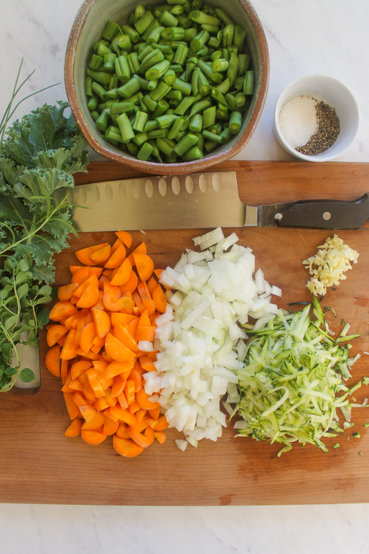 Chopped vegetables on a cutting board and a bowl of chopped green beans.