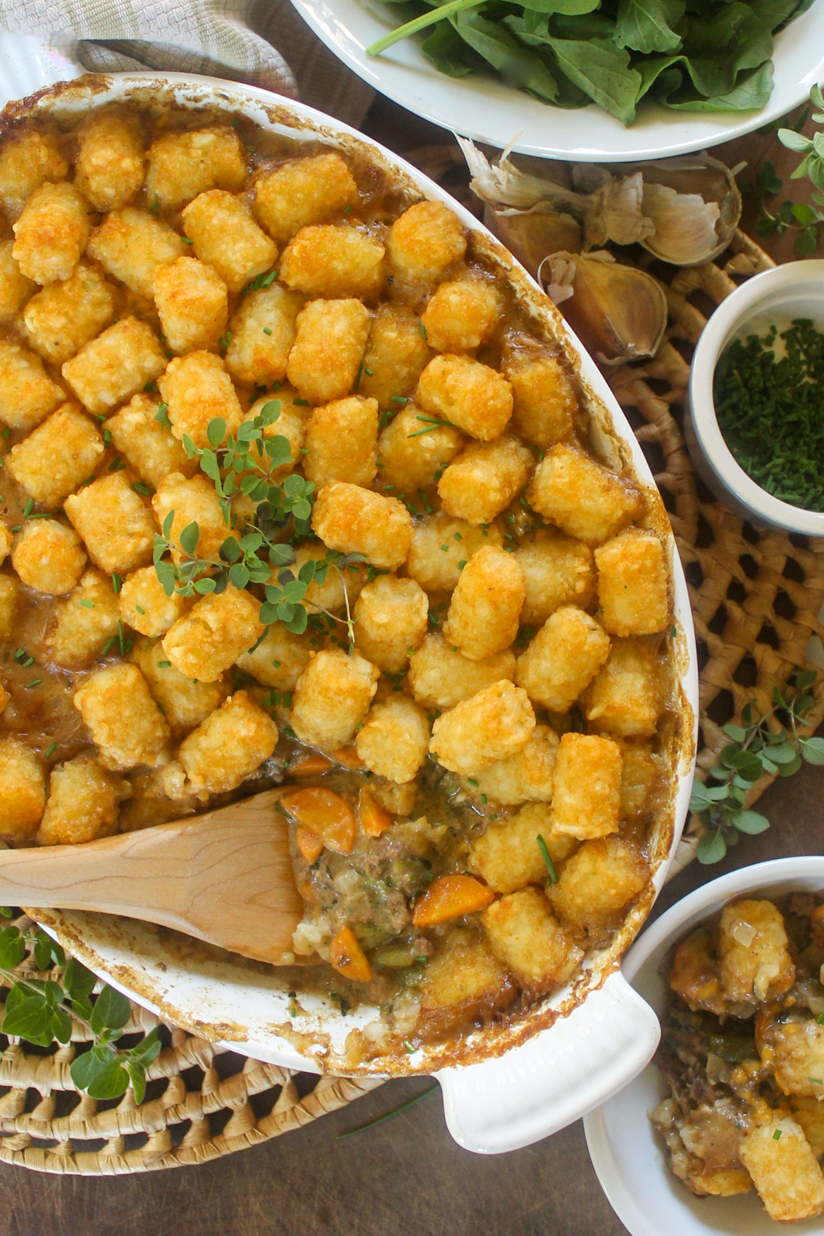 A casserole dish of tater tot hot dish served with a wooden spoon.