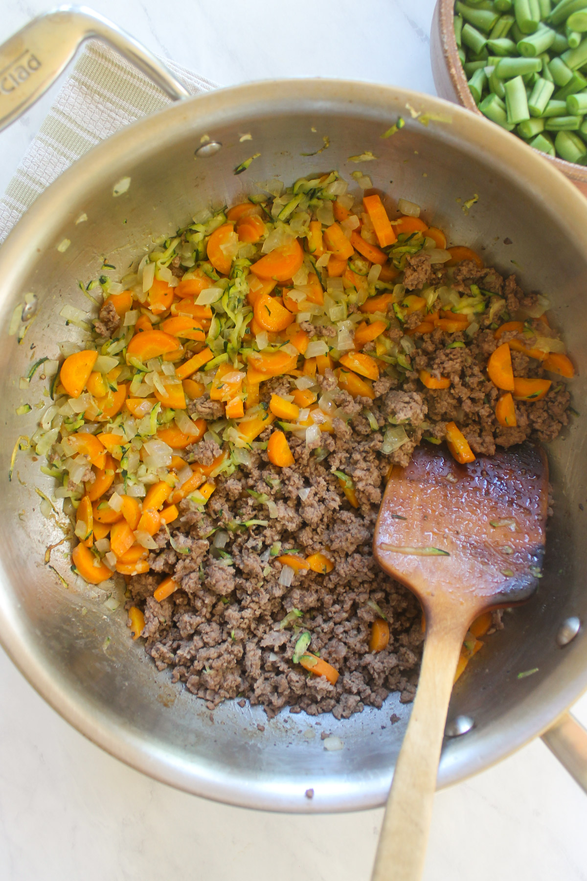 Browned ground beef in a skillet with sautéed carrots, onion and zucchini.