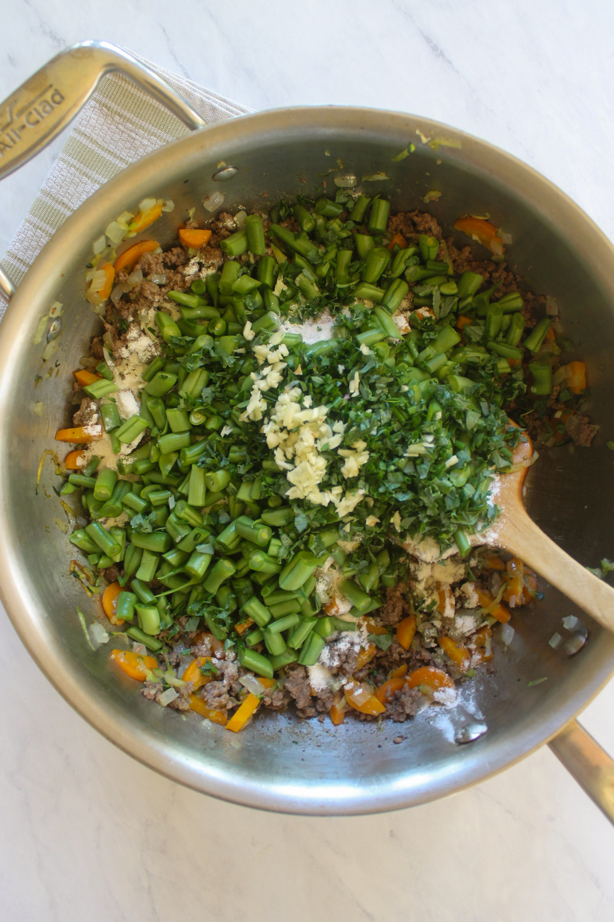 Adding green beans, herbs, garlic, and flour to the cooked beef and vegetables.