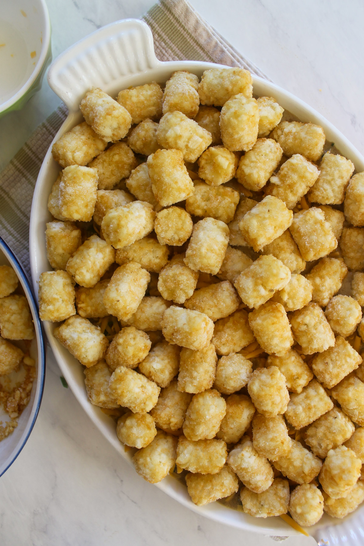 A dish of unbaked tater tot casserole with frozen tater tots.