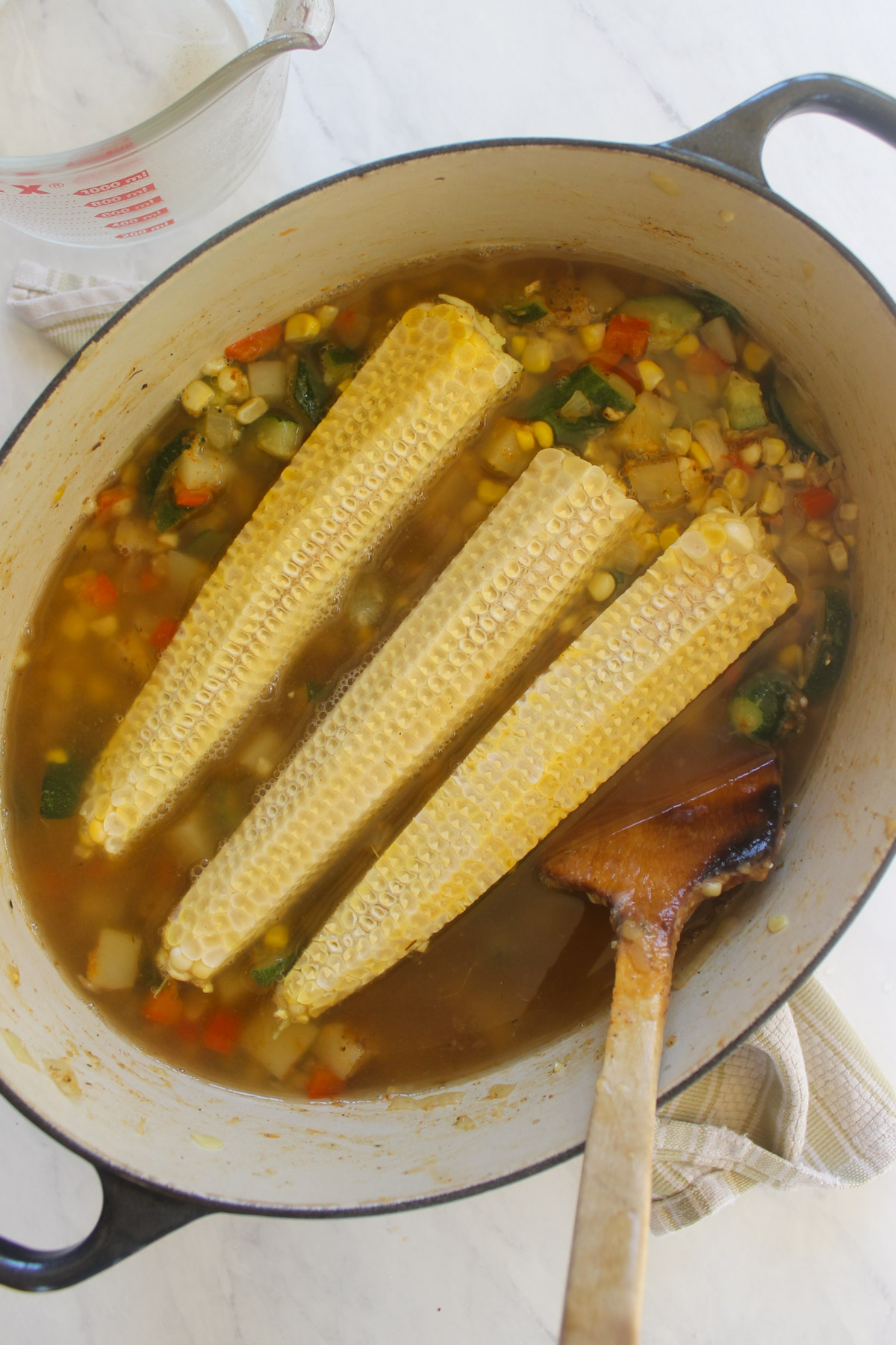 Three corn cobs simmering in a pot of soup.