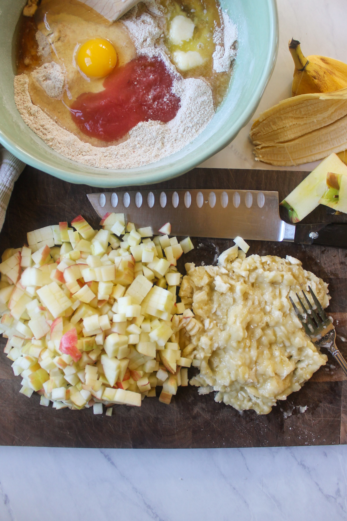 Chopped apples and mashed banana on a cutting board.