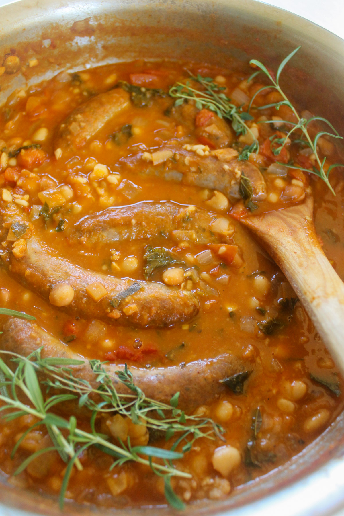 Italian sausage links in a tomato white bean broth with rosemary sprigs.