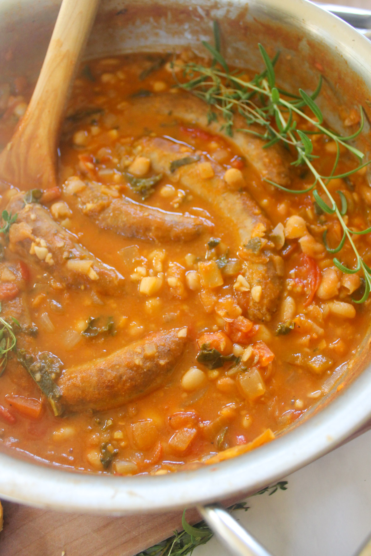 White bean tomato sausage cassoulet in a skillet with a wooden spoon.