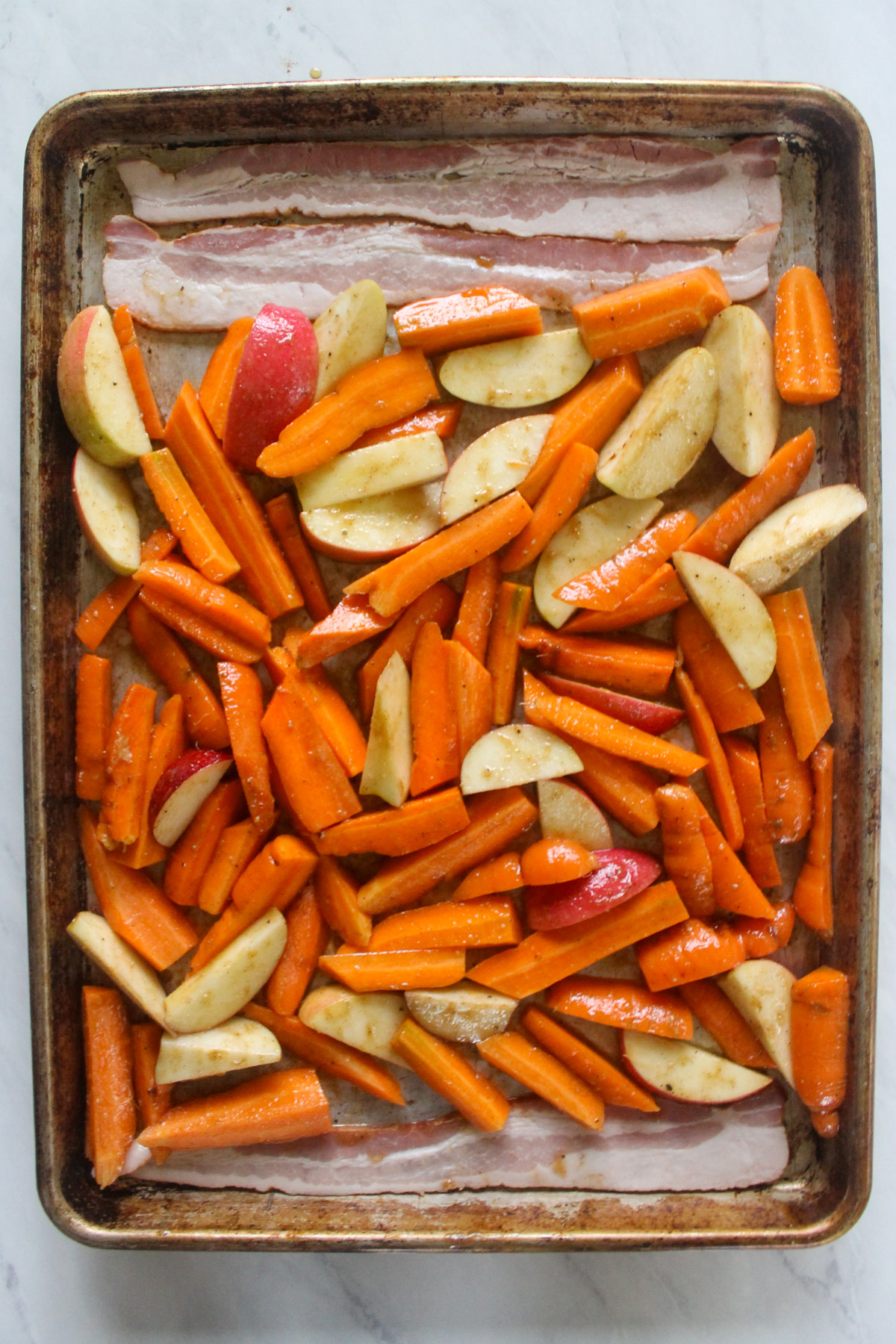 Raw bacon, carrots and apples tossed in maple glaze on a sheet pan.