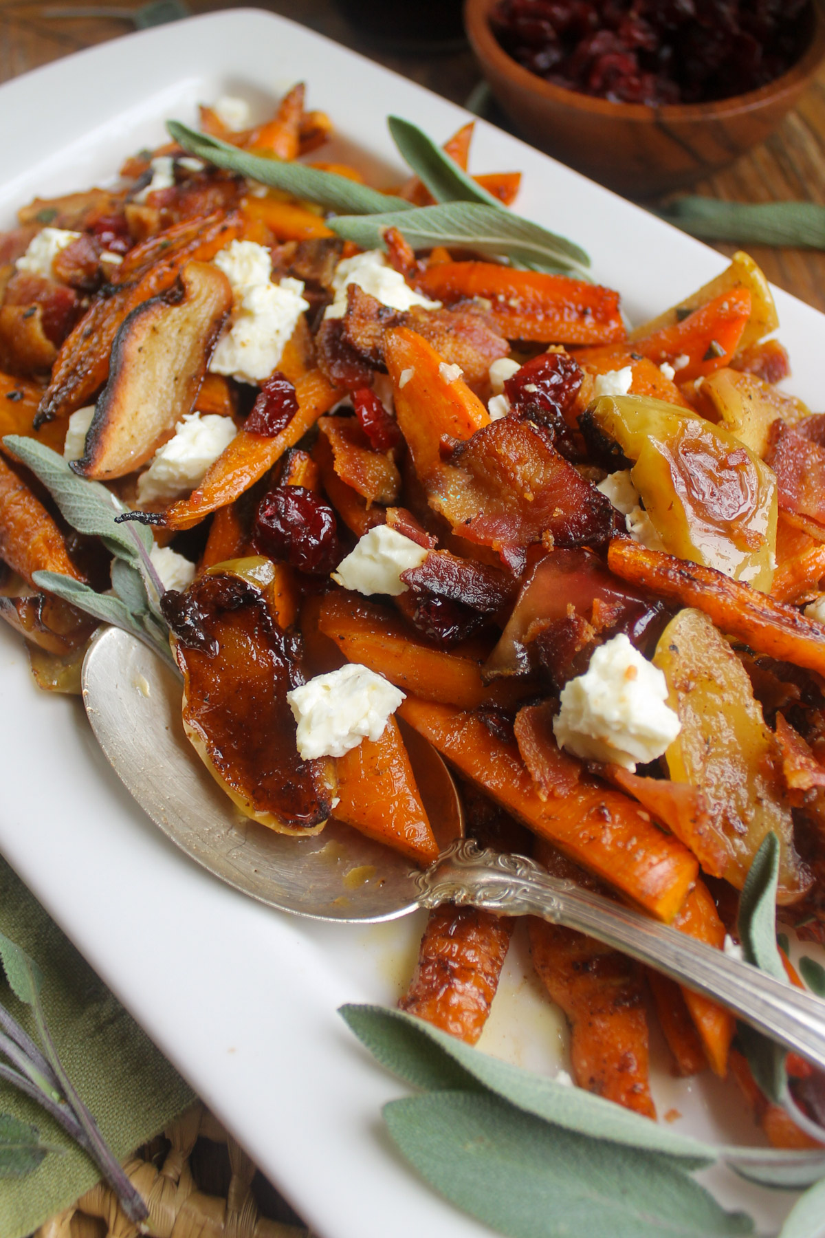 A white platter of roasted carrots and apples with bacon and sage.