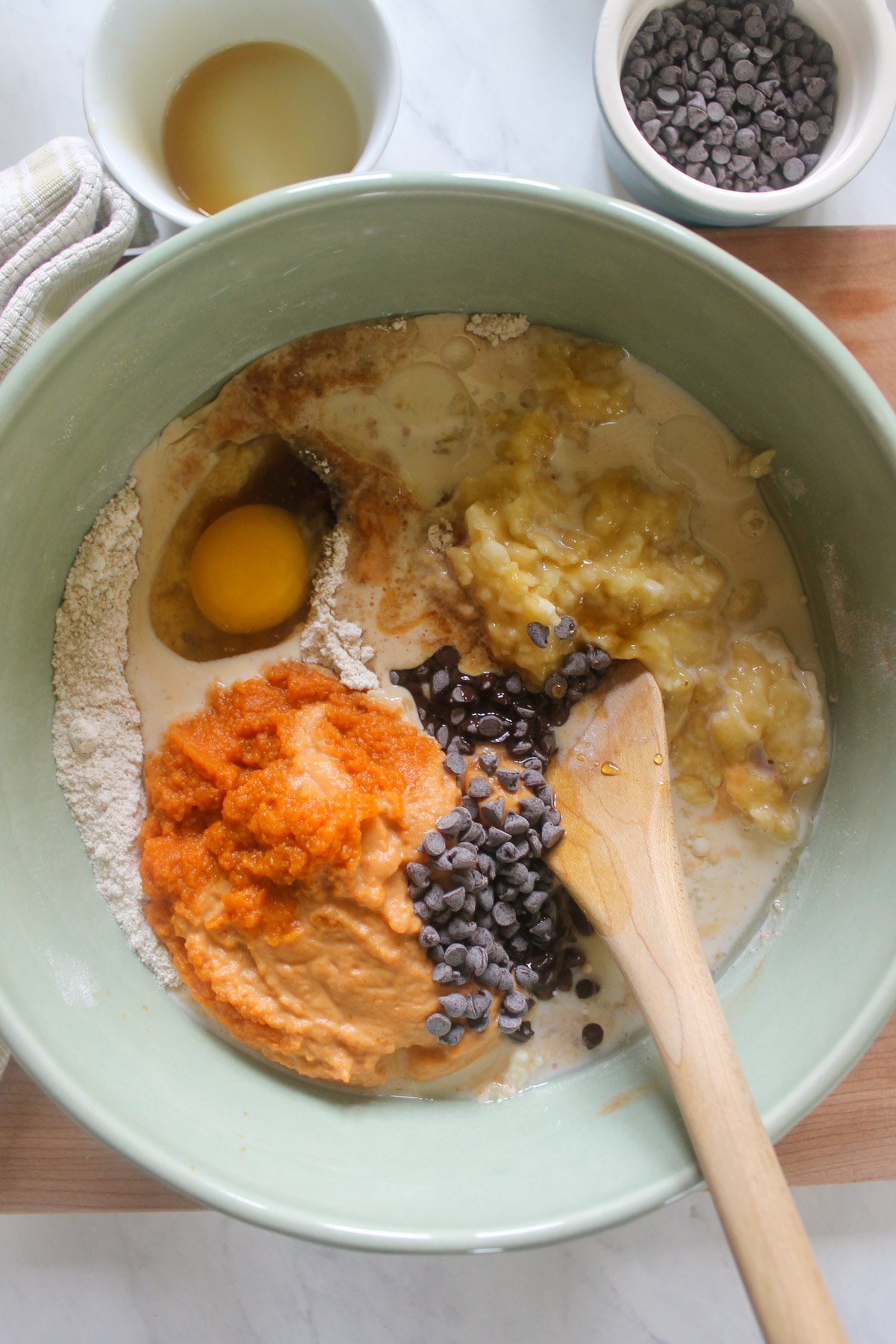 Ingredients for pumpkin banana muffins in a bowl with a wooden spoon.