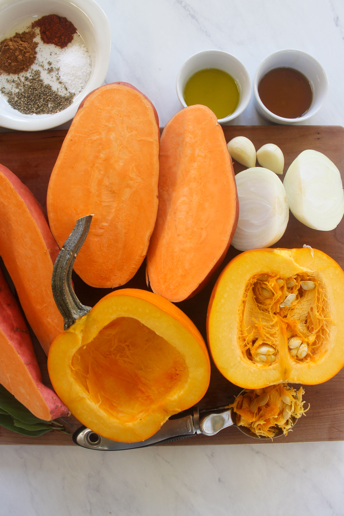 Sweet potatoes and pumpkin cut in half on a cutting board with onions and garlic.