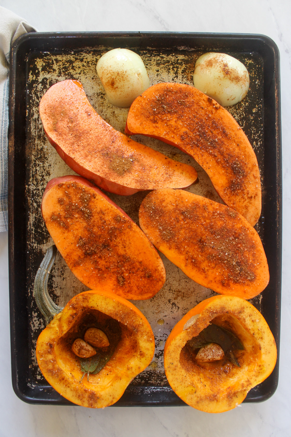 Pumpkin and sweet potato halves on a large sheet pan with spices.