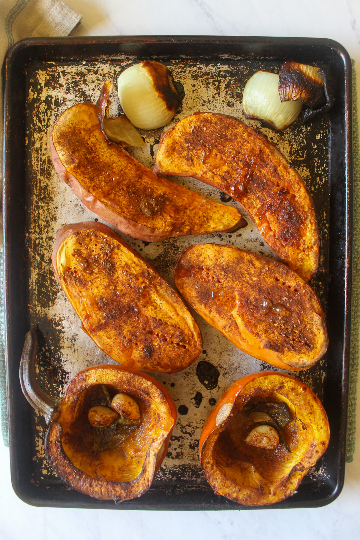 Baked pumpkin and sweet potato halves on a sheet pan.