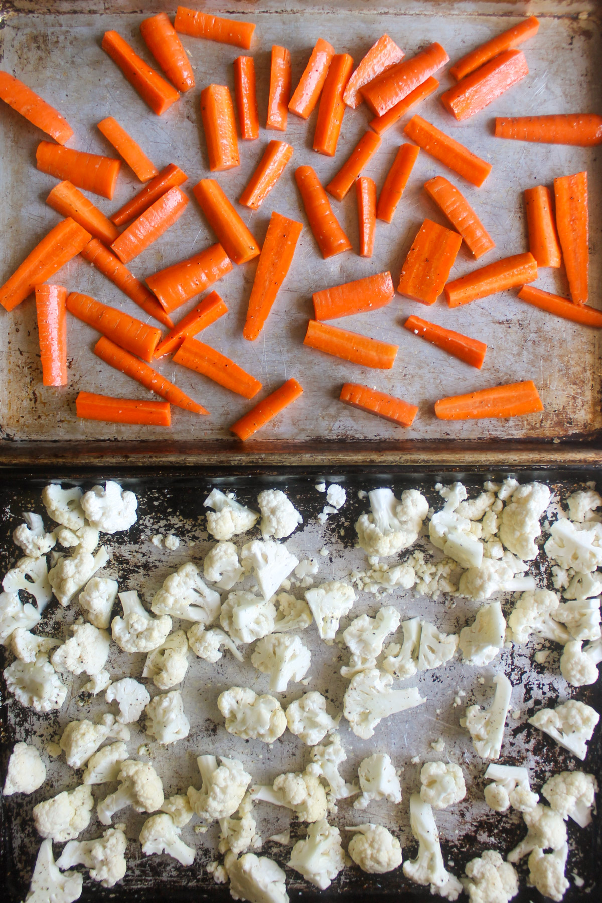 Raw carrots and cauliflower spread on two large sheet pans.