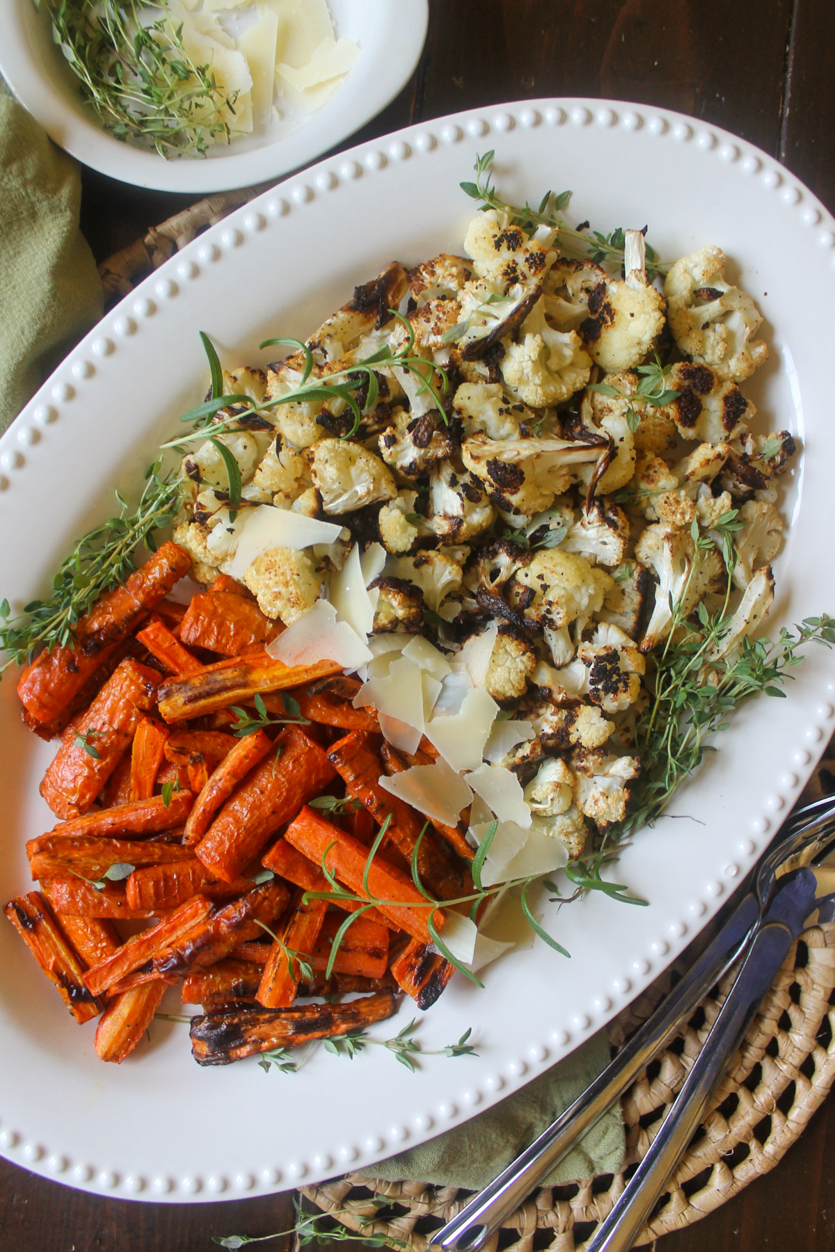 A white platter of roasted carrots and cauliflower with fresh herbs.