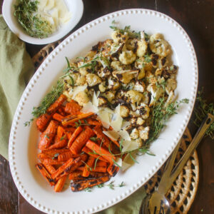 Roasted cauliflower and carrots on a white dish with shaved Parmesan cheese.