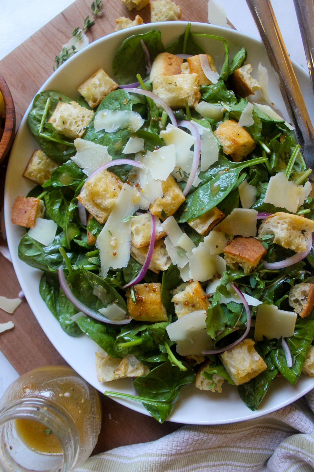 A white plater of tossed spinach arugula salad with red wine vinaigrette.